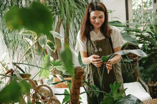 A woman in an apron tending to plants in a lush, sunlit greenhouse.