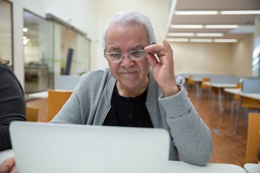 Elderly man using a laptop in a classroom setting, learning new technology skills.