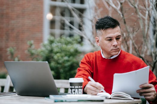 Focused professional working with laptop and documents at outdoor cafe, illustrating modern remote work culture.