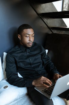 Man in black shirt using a laptop in a stylish indoor workspace.